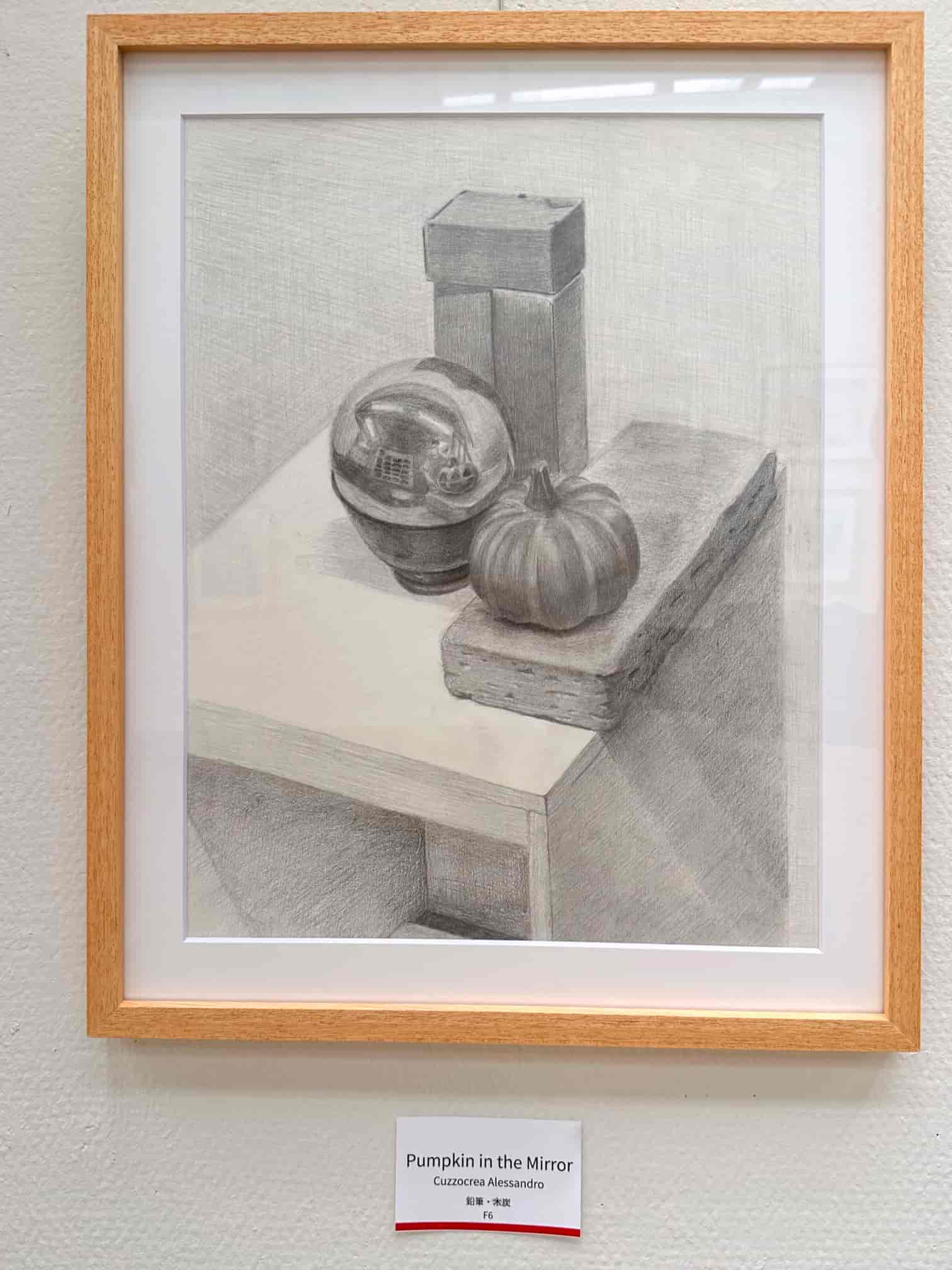 Graphite still life drawing titled 'Pumpkin in the Mirror' by Alessandro Cuzzocrea, displayed at an art exhibition